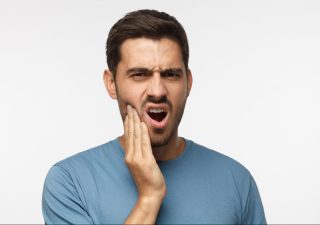 Adult man with beard holding side of face in pain hudsonville mi dentists
